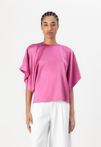 Fuchsia satintopp med løse batwing-ermer og rund hals, kombinert med hvite brede bukser. Glatt, skinnenede tekstur.