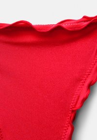 Top bikini rosso con bordo ondulato. Tessuto liscio, forma triangolare e dettagli di cuciture elastiche lungo le cuciture.