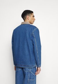 Blauwe denimjacket met een beige corduroy kraag, met een relaxte pasvorm en zichtbare stikdetails. Draagt men met bijpassende denim broek.