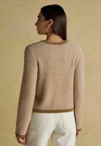 Beež kudumissviiter, millel on kalasaba muster, ümardatud kaeluse ja pruuni äärega. Koos heledate kõrge vöökohaga pükste jaoks.