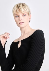Black ribbed long-sleeve top with an off-shoulder design and a keyhole detail at the neck, featuring a small silver hardware accent.