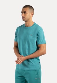 T-shirt in cotone turchese con colletto girocollo, maniche corte e un piccolo etichetta del marchio sul petto; texture morbida, vestibilità casual.