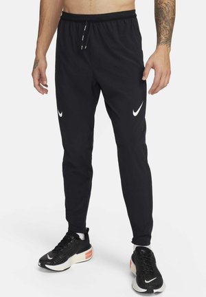 Pantalones de chándal negros de Nike con cintura elástica, cordón y acentos de logo en blanco. Diseño de corte ajustado, tejido ligero y textura suave.