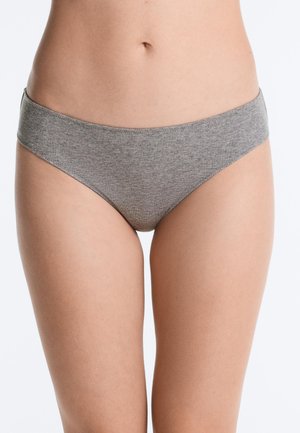 Torace femminile che indossa biancheria intima grigia a coste in stile bikini, in piedi su sfondo bianco semplice.