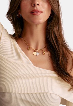 Gold chain necklace featuring various charms, including a silver star and a round pendant, against a ribbed, off-white top.
