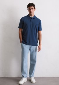 Navyblauwe polo met een kraag en korte mouwen, gecombineerd met lichtblauwe rechte jeans en witte Sneakers. Eenvoudig, casual ontwerp.