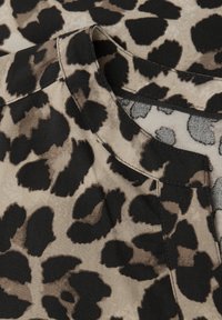 Tkanina s leopardím vzorem obsahující velké černé skvrny na světle hnědém pozadí. Obsahuje kulatý výstřih a hladkou strukturu.