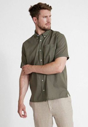 Camicia verde oliva a maniche corte realizzata in tessuto strutturato, dotata di colletto button-down, taschino anteriore e cinque bottoni bianchi sul fronte.