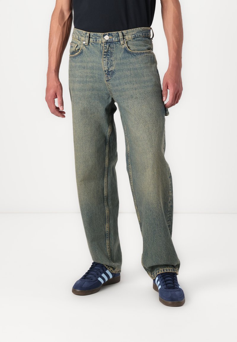 Light blue denim jeans with a relaxed fit, featuring five pockets, a button closure, and slightly faded texture. Paired with blue sneakers.
