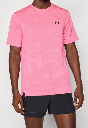 Mann trägt ein leuchtend pinkes, kurzärmeliges Sportshirt und schwarze Sportshorts, steht vor einem neutralen Hintergrund.