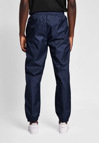 Navy vindjacka byxor med elastisk midja och mudd, med en slät, glänsande yta och en avslappnad passform, tillsammans med vita sneakers.