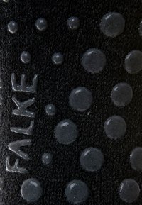 Calcetín negro de punto con puntos de agarre de silicona redondeados y detalle de logo en relieve, que ofrece textura y funcionalidad antideslizante.