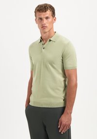 Lichtgroen poloshirt van textuurstof, met een drieknopenlijst en geribbelde manchetten. Opvallend logo detail nabij de zoom.