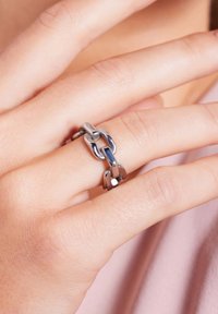 Zilverkleurige ring met in elkaar grijpende kettingschakels. Gladde, gepolijste afwerking met een combinatie van lichte en donkere metalen elementen.