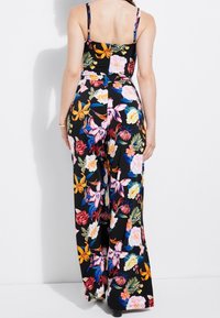 Blommig jumpsuit med justerbara spaghettistappar, med svart bakgrund, livfulla flerfärgade blommor och vid ben-design. Strukturerad tyg.