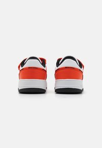 Red and white sneakers with a smooth leather upper, padded black lining, and textured rubber outsole. Rear view highlights design details.