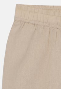 Gros plan sur un tissu en lin beige présentant une ceinture élastique avec une texture froncée et une surface lisse, mettant en avant un minimum de plis.