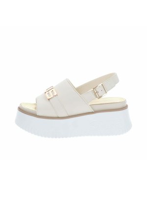 Sandale plateforme beige à bout ouvert avec semelle blanche épaisse, bride de cheville réglable avec boucle dorée et accent décoratif doré sur la bride avant.