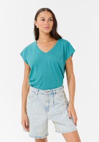 Tyrkysový v-neck top s krátkým rukávem vyrobený z měkkého materiálu, spárovaný s světlými vysoce pasovými džíny s klasickým pětikapsovým designem.