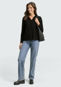 Schwarzes Langarmoberteil mit V-Ausschnitt, kombiniert mit hellblauen geraden Jeans und schwarzen Plateau-Stiefeln, hält eine schwarze Ledertasche.