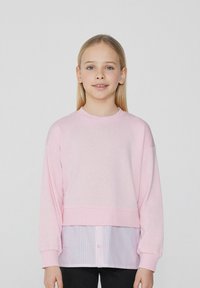Rosa verkürzter Sweater mit langen Ärmeln über einem blau-weiß gestreiften Hemd. Glatte Textur, runder Ausschnitt und lässige Passform.