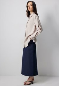 Light beige long-sleeve button-up shirt with a relaxed fit, paired with a dark navy ankle-length skirt and black strappy heels.