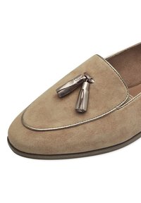 Mocassino in suede beige con punta arrotondata e dettaglio di nappina metallica. Cuciture a contrasto e superficie liscia e testurizzata.