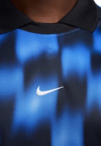 Nike sportshirt met een blauw en zwart verlooppatroon, textuurstof en een wit logo op de linkerborst. Zwarte kraag.