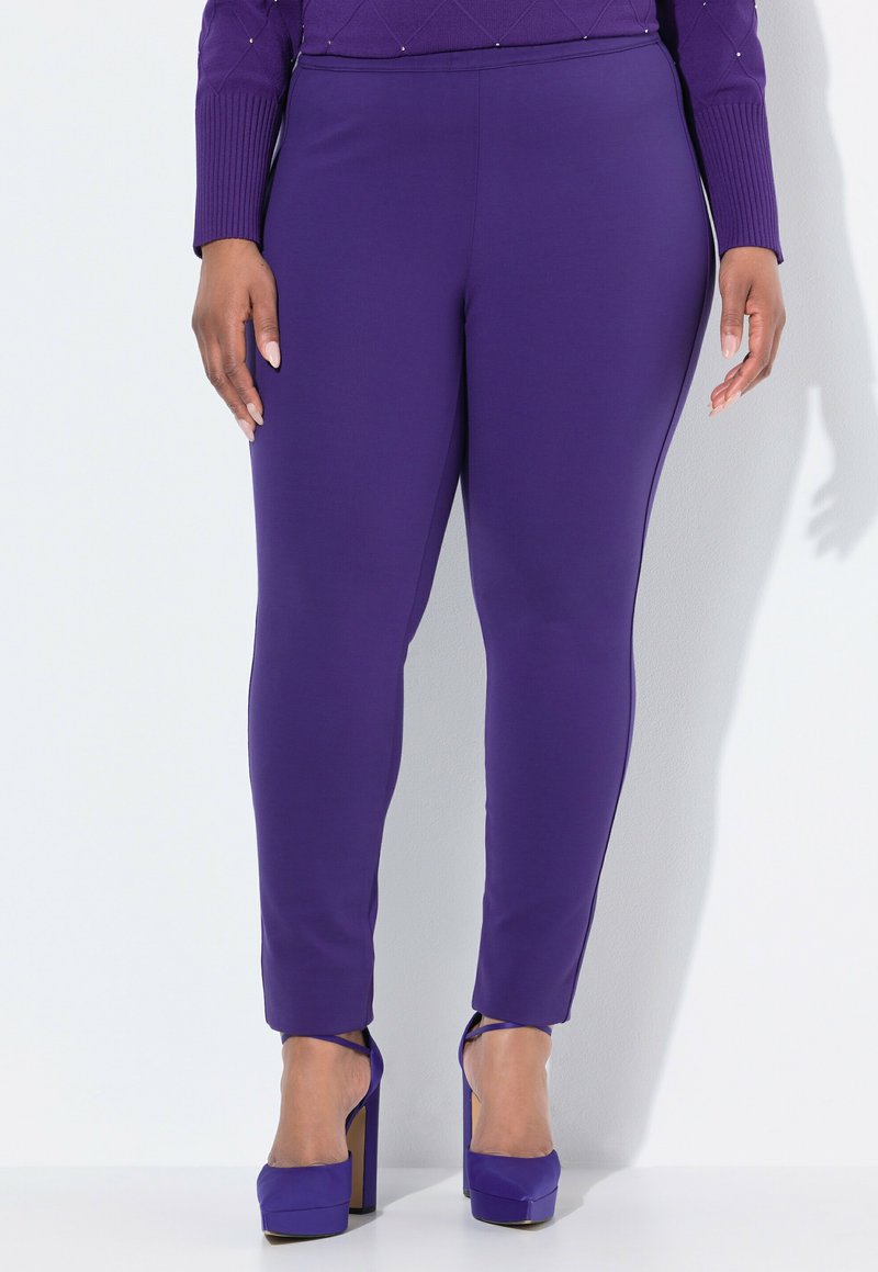 Lila stretchleggings med slät textur, utrustade med midja i midjehöjd och avsmalnande passform. Matchas med lila högklackade skor.