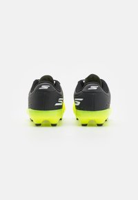Botas de fútbol negras y amarillas neón con parte superior texturizada, diseño bajo, logo prominente y tacos de goma para tracción.