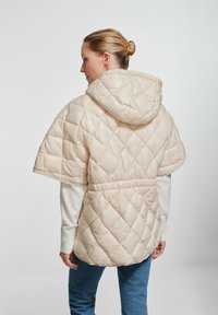 Beżowy pikowany ponczo z kapturem, krótkimi rękawami, elastycznym paskiem w talii oraz gładką fakturą. Wzór z wkładkami w kształcie diamentów.