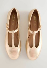 Par de zapatos planos metálicos dorados con tiras en T y cierre de hebilla, marca NEXT, talla 6½/40, exhibidos sobre un fondo claro y liso.