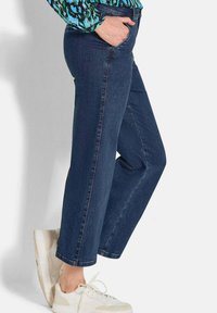 Jean en denim bleu foncé avec une coupe décontractée, jambe droite et poches latérales. Associés à des baskets blanches avec un dessus texturé et des lacets.