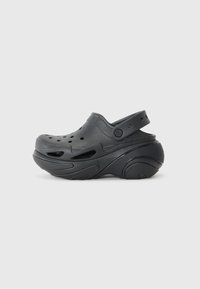 Black clog made from flexible synthetic material, featuring ventilation holes and a back strap. Rounded toe and textured sole for grip.