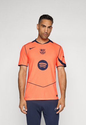 Un maillot de football orange avec des accents noirs, présentant un col rond, le logo de l'équipe sur la poitrine, et un logo Spotify circulaire bien en évidence au centre.