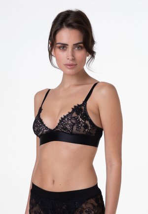 Bralette in pizzo nero con forma triangolare, tessuto trasparente, bordi a scallop e una fascia sottostante in satin liscio. Spalline semplici e regolabili.