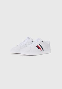 Witte sneakers met een gladde canvas bovenkant, voorzien van rode en blauwe accenten, ronde neus en platte rubberen zool. Vetersluiting.