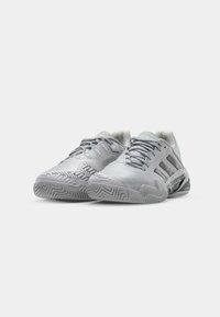 Helle graue Sportschuhe mit strukturiertem Mesh-Obermaterial, Gummisohle mit Zickzackmuster und drei Streifen-Branding an den Seiten.
