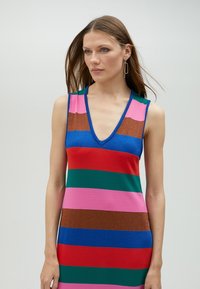 Ärmlänkt klänning med djup V-ringning, som har breda horisontella ränder i rosa, röd, grön, blå och brun; materialen har en glansig textur.