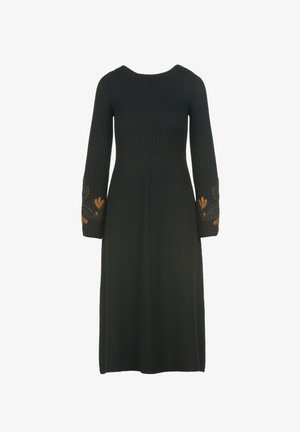 Juoda megzta suknelė su prigludusia viršutine dalimi, ilgos mėgstinės rankovės, dekoruotos auksiniais išsiuvinėjimais. A-formos siluetas, iki kelių.