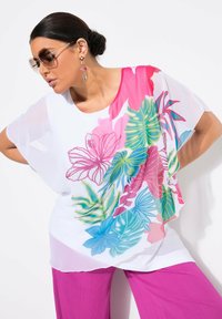 Luftig hvid bluse med livlige pink, grønne og blå tropiske blomsterprints. Sammen med lyserøde plisserede bukser og oversized solbriller.