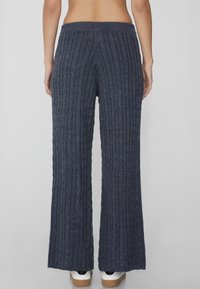 Pantalones de pierna ancha en gris oscuro de punto trenzado, con una cinturilla acanalada. La textura de la tela es suave y gruesa. Sin hardware ni patrones visibles.
