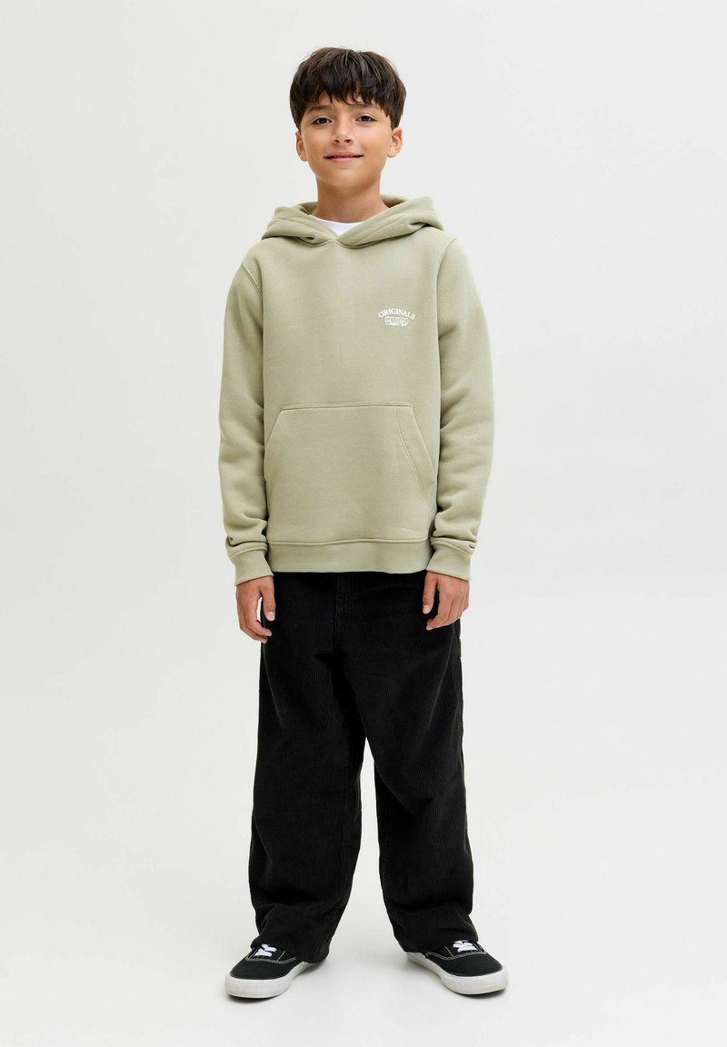 Felpa verde chiaro con tasca a marsupio e logo bianco sul petto, abbinata a pantaloni in corduroy neri e sneaker nere.