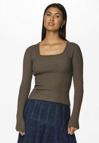 Prążkowany, długi sweter w ciemnooliwkowym kolorze z kwadratowym dekoltem, dopasowanym krojem i teksturowanym materiałem. Połączony z ciemnoniebieską spódnicą.