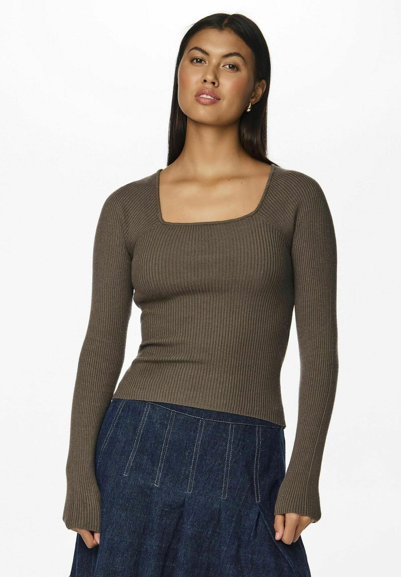 Prążkowany, długi sweter w ciemnooliwkowym kolorze z kwadratowym dekoltem, dopasowanym krojem i teksturowanym materiałem. Połączony z ciemnoniebieską spódnicą.