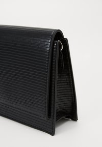 Clutch nero con texture e design strutturato, presenta una finitura lucida e una patta pieghevole. Componenti in metallo argentato inclusi.