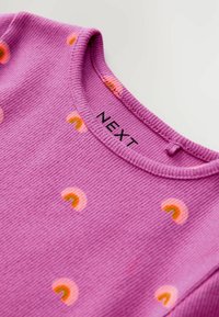 Haut en tissu côtelé violet avec des motifs arc-en-ciel. Il possède un col rond et une couture subtile. L'étiquette indique "NEXT". Texture douce sur l'ensemble.