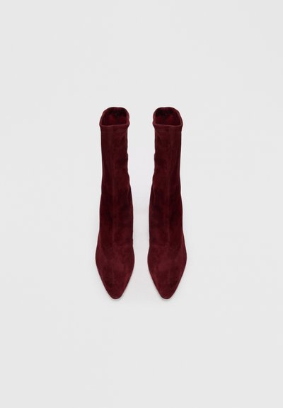 Bottines en daim bourgogne avec un bout pointu et un dessus ajusté et doux qui s'étend au-dessus de la cheville. Texture lisse, design minimaliste.