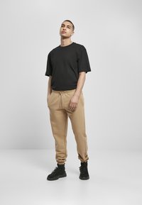 Svart T-skjorte med kort erme kombinert med beige joggebukser, med elastisk midje og ribbestrikkede ankler, iført svarte støvler.