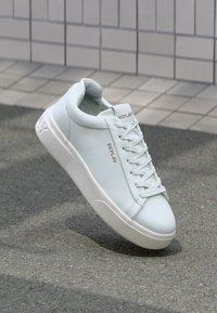 Zapatillas blancas de cuero con un acabado texturizado, puntera redonda y cordones a juego. Presentan un sutil logo "REPLAY" en dorado en el lateral.